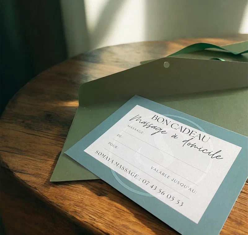 Le bon cadeau Somaya Massage et son enveloppe, posés sur une table.