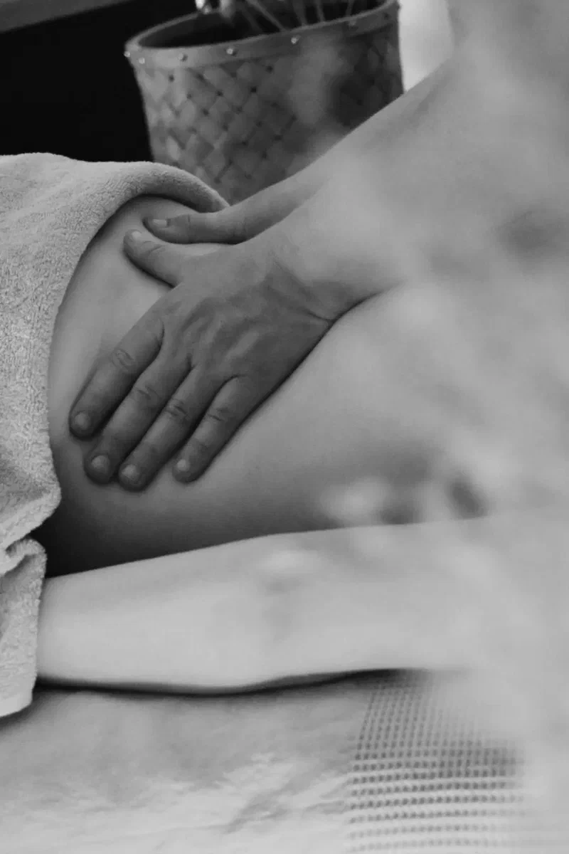Les mains de Stecy réalisent un massage du dos, en noir et blanc